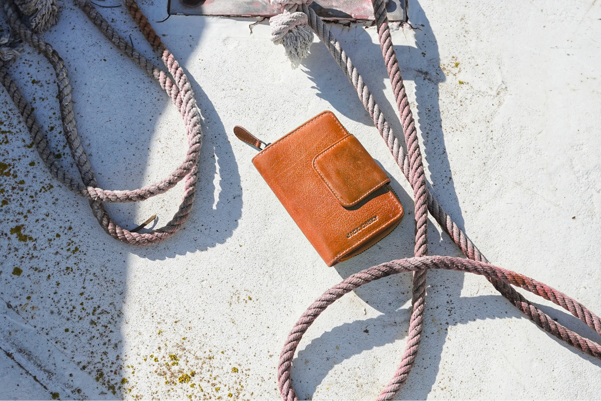 Eine braune Jack Kinsky Geldbörse, sie liegt auf dem Boden, wahrscheinlich an einem Hafen. Um die Börse herum ist ein Tauseil.